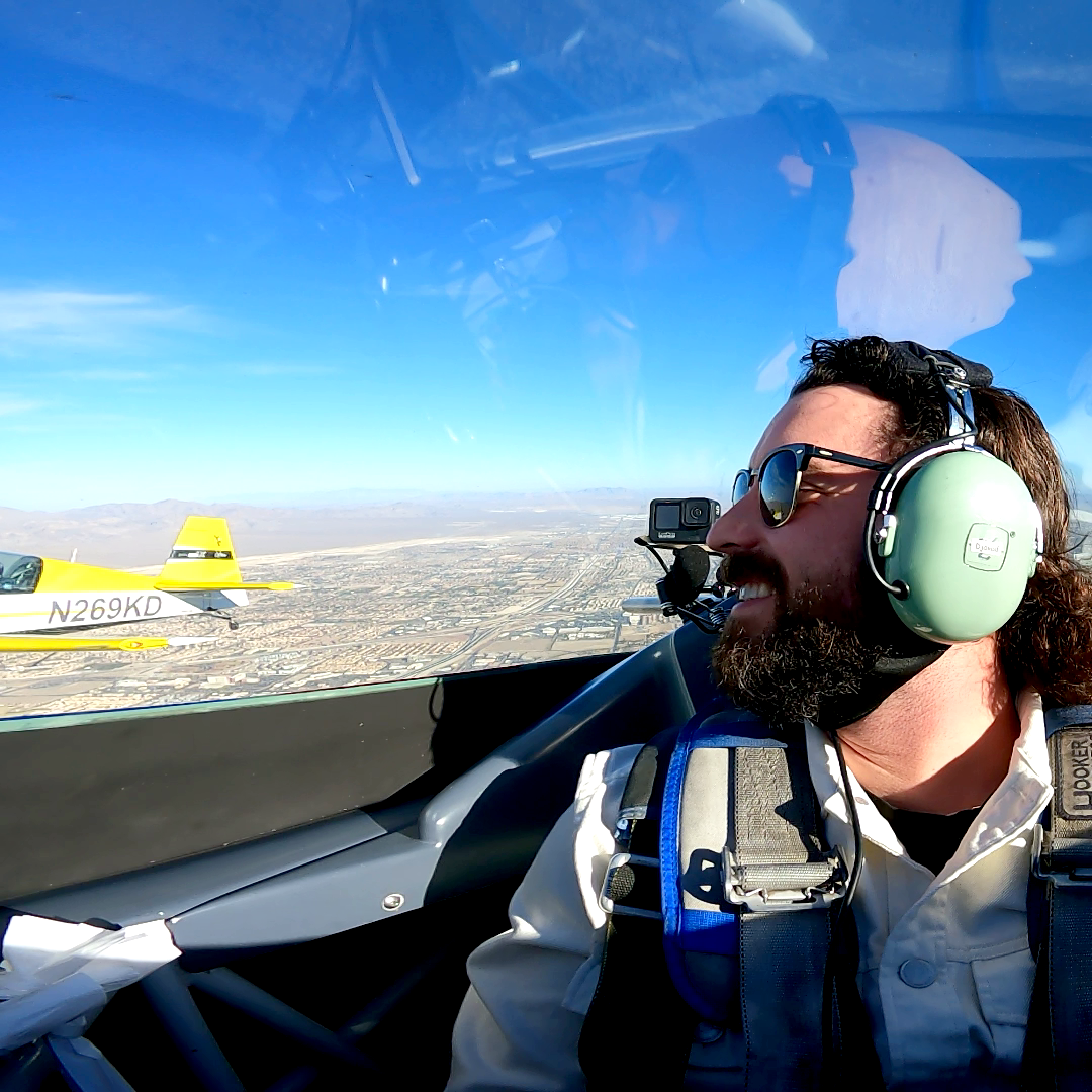 A man wearing headphones and sunglasses looks out the window of a plane with the number 0 on it