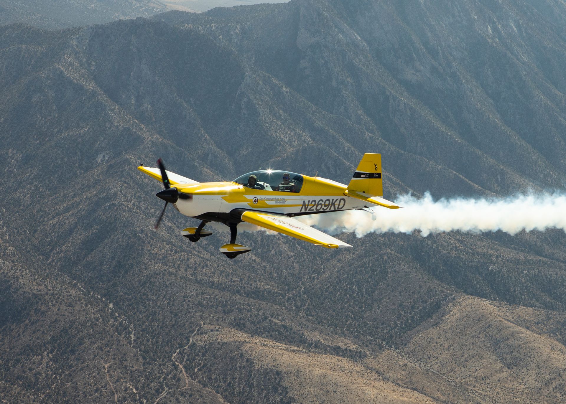 A yellow and white plane with the letters n55012 on the tail is flying over mountains