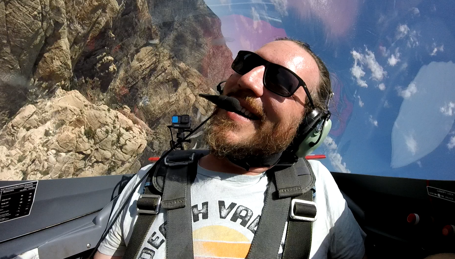 A man wearing headphones and sunglasses is sitting in a plane