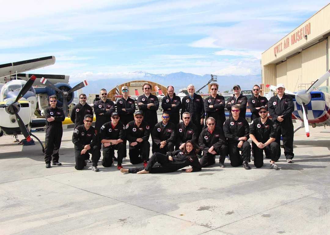 A group of people are posing for a picture in front of an airplane hangar.