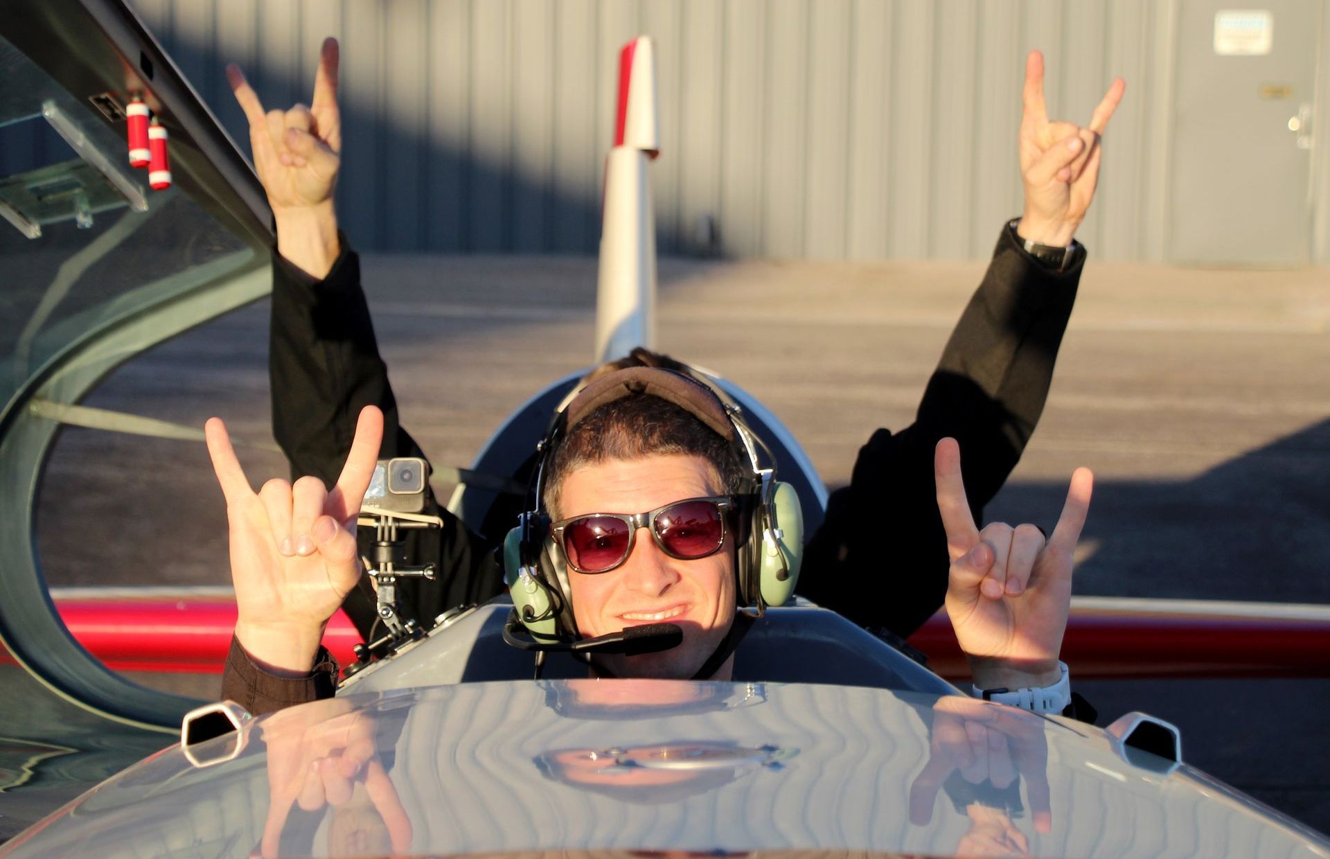 A man wearing headphones and sunglasses is giving the horns up sign