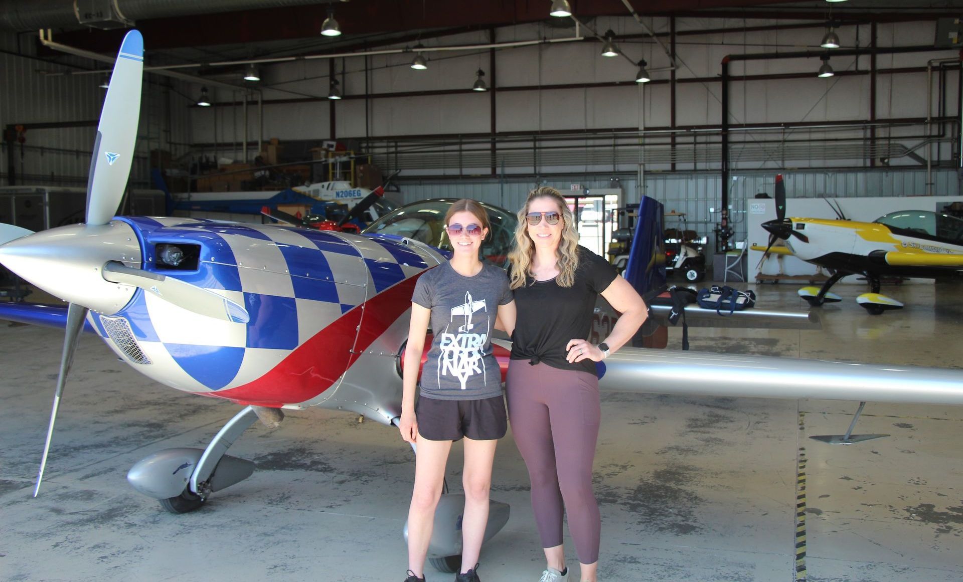 Two women standing in front of a plane in a hangar