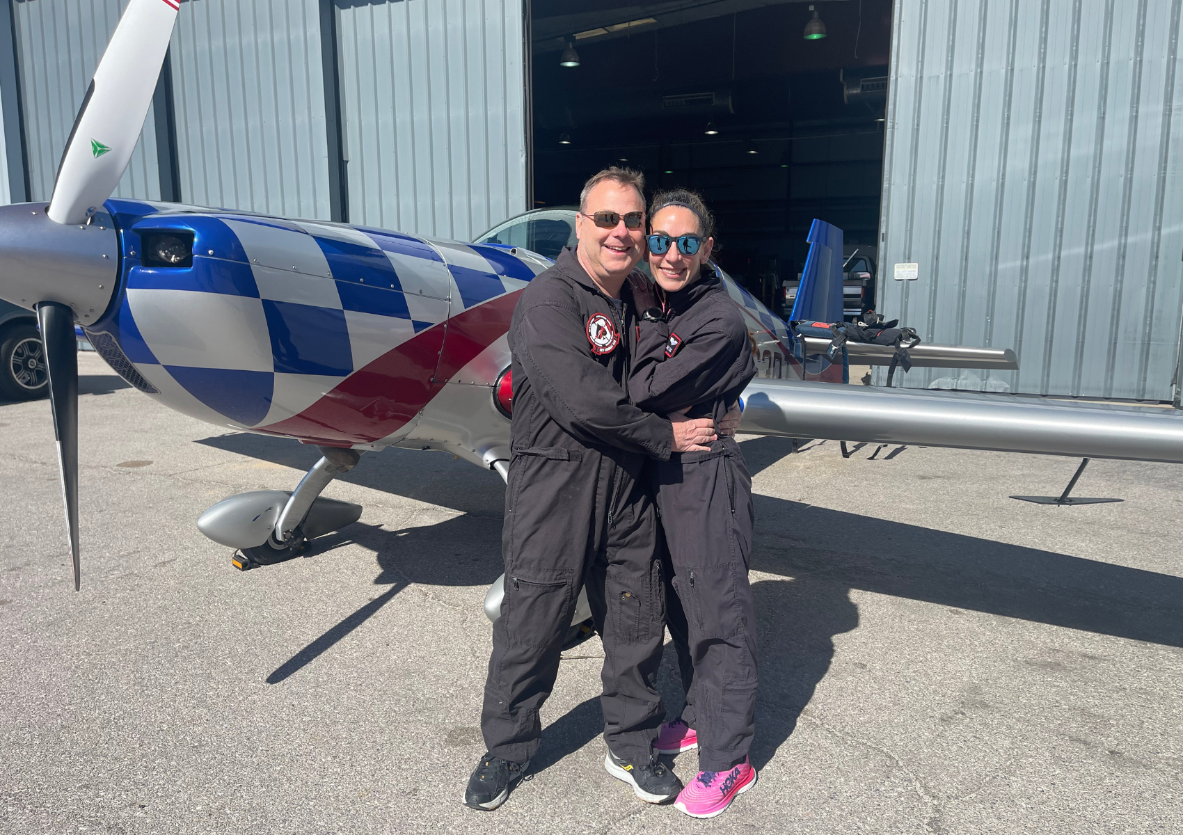 A man and a woman are hugging in front of an airplane.