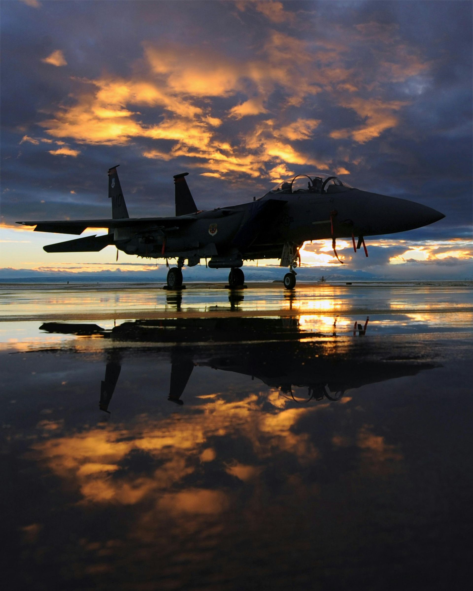 A fighter jet is parked on a wet runway at sunset