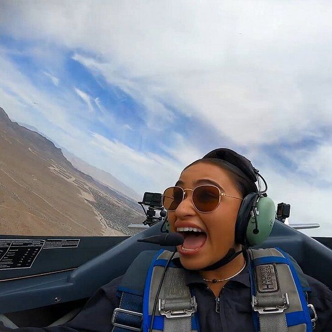 A woman wearing headphones and sunglasses is flying a plane