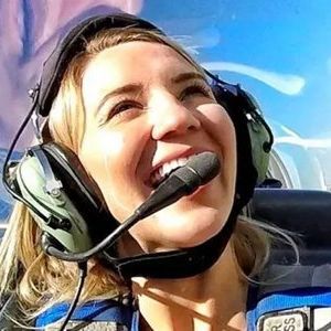 A woman wearing headphones and a microphone is smiling in an airplane.