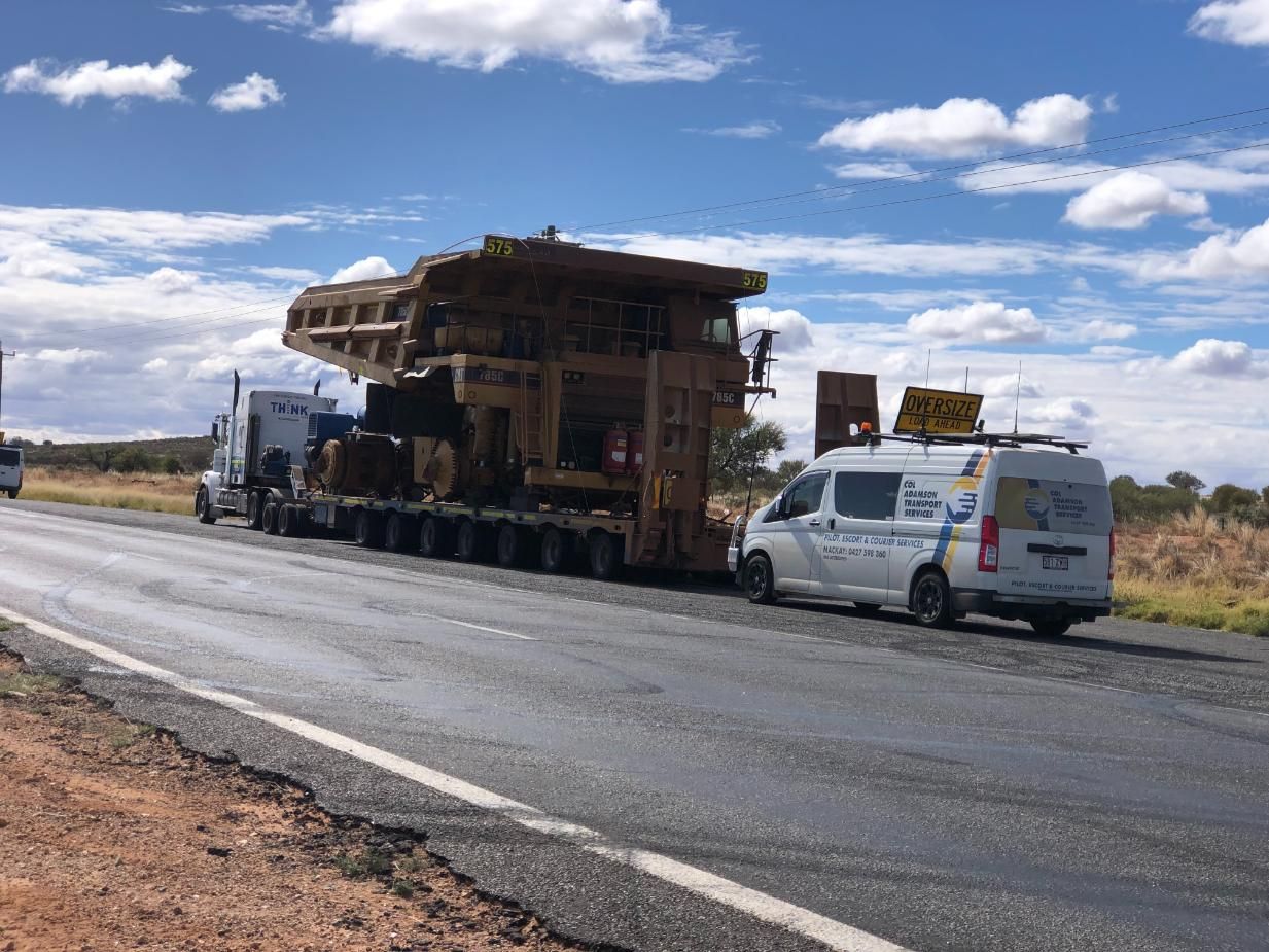 A White Van Is Parked on The Side of The Road Next to A Large Truck — Col Adamson Transport Pilot Services In Farleigh, QLD