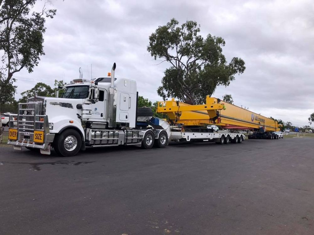 A White Semi Truck is Carrying a Large Yellow Crane on a Trailer — Col Adamson Transport Services in Farleigh, QLD