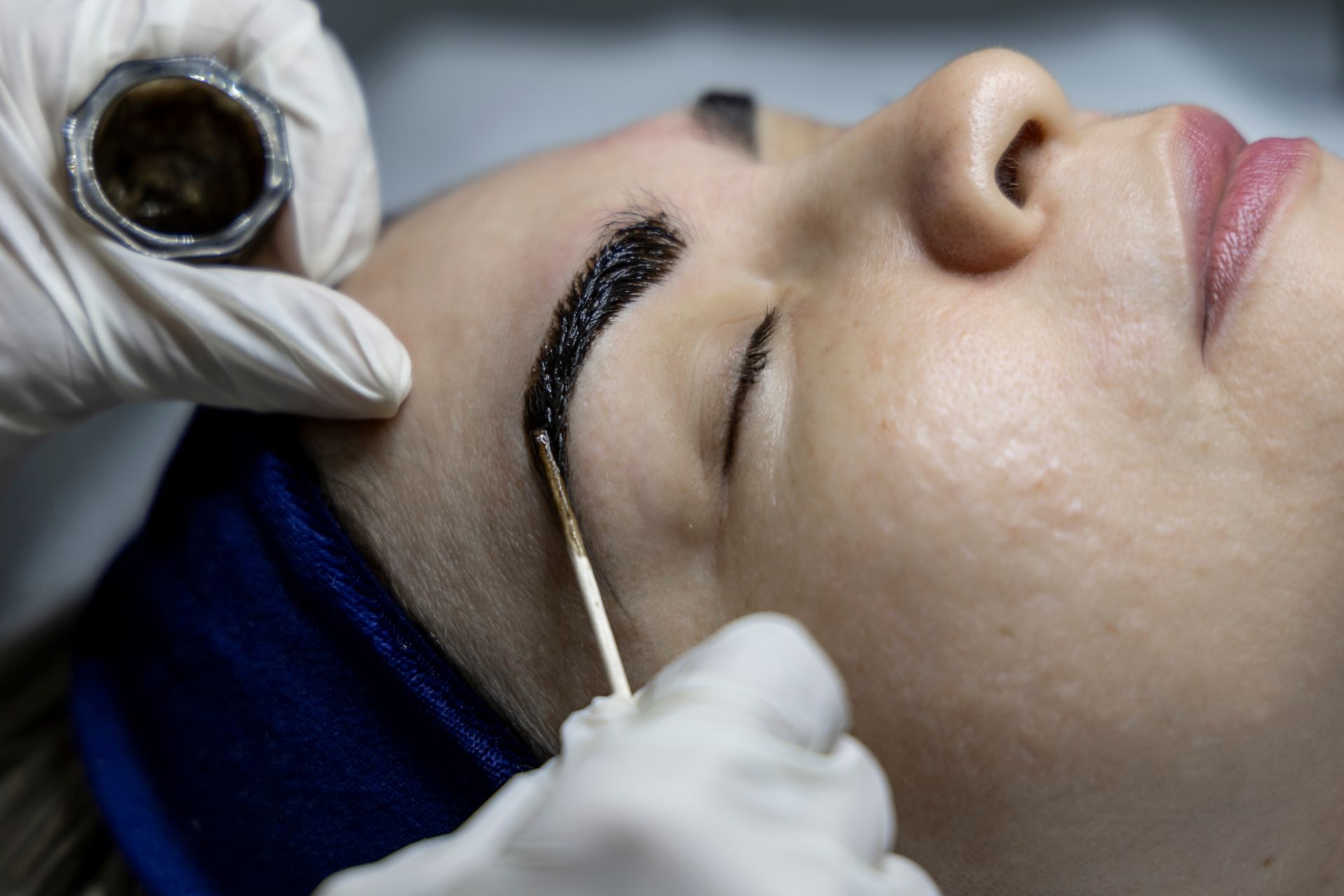 A person getting their eyebrow tattooed by a gloved technician with a tool, close-up.