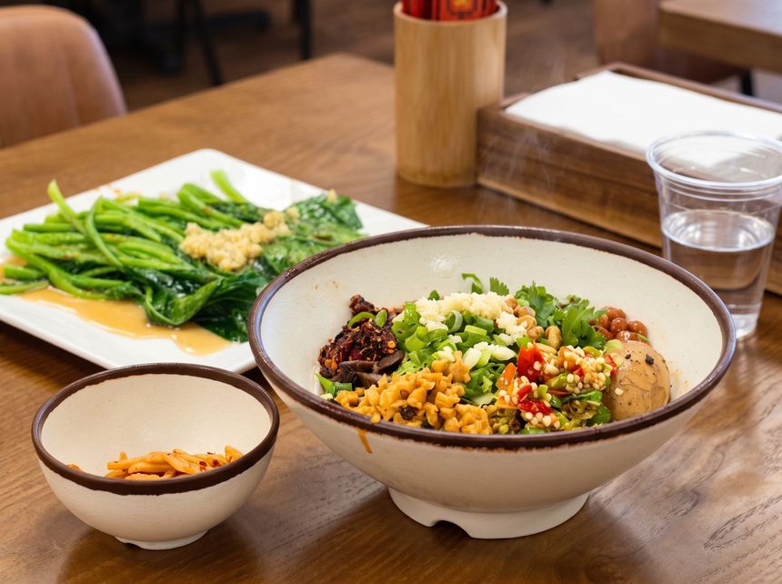 Bowl of colorful mixed vegetables and grains on a wooden table with side dishes and a drink