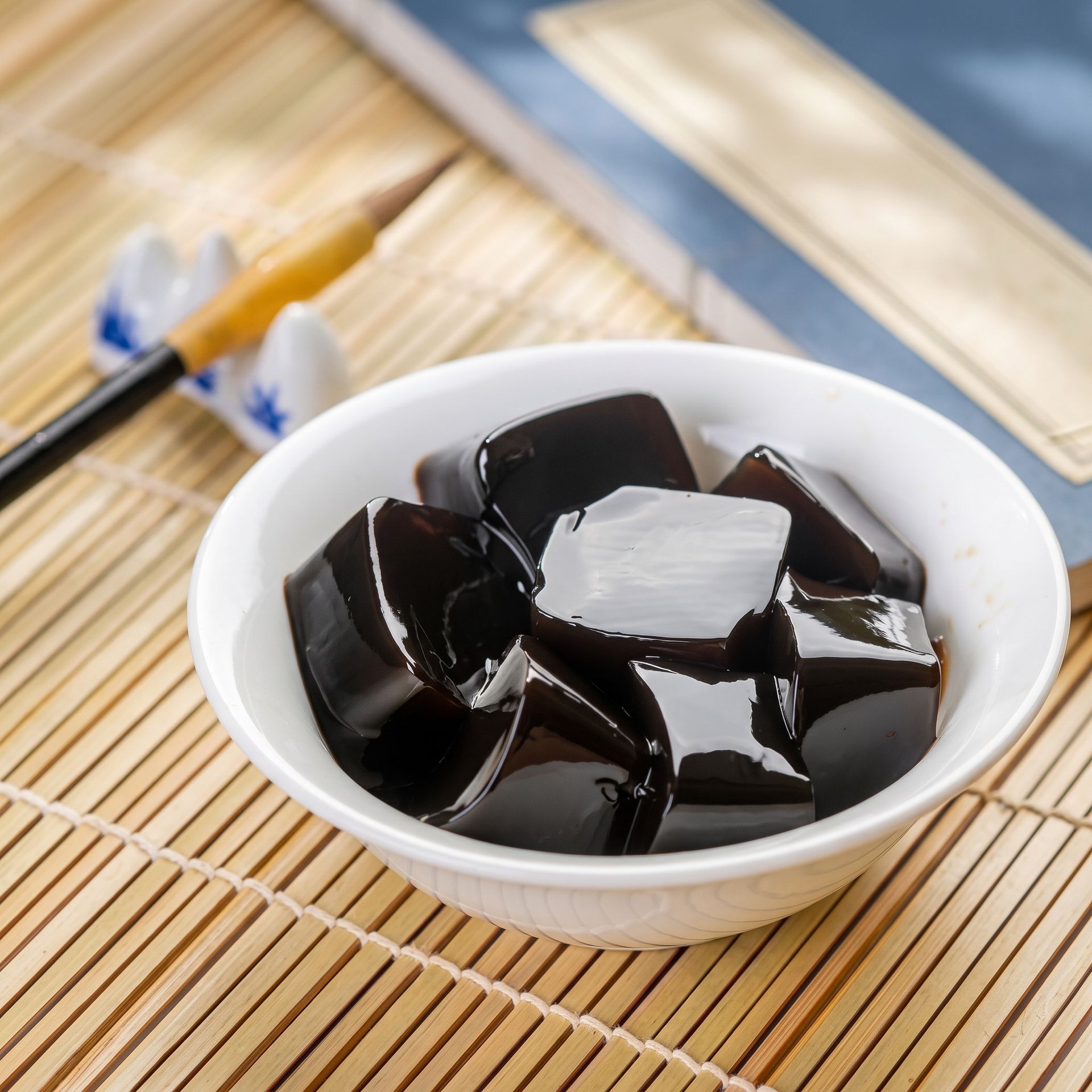 White bowl of black jelly cubes on a bamboo mat, with chopsticks nearby