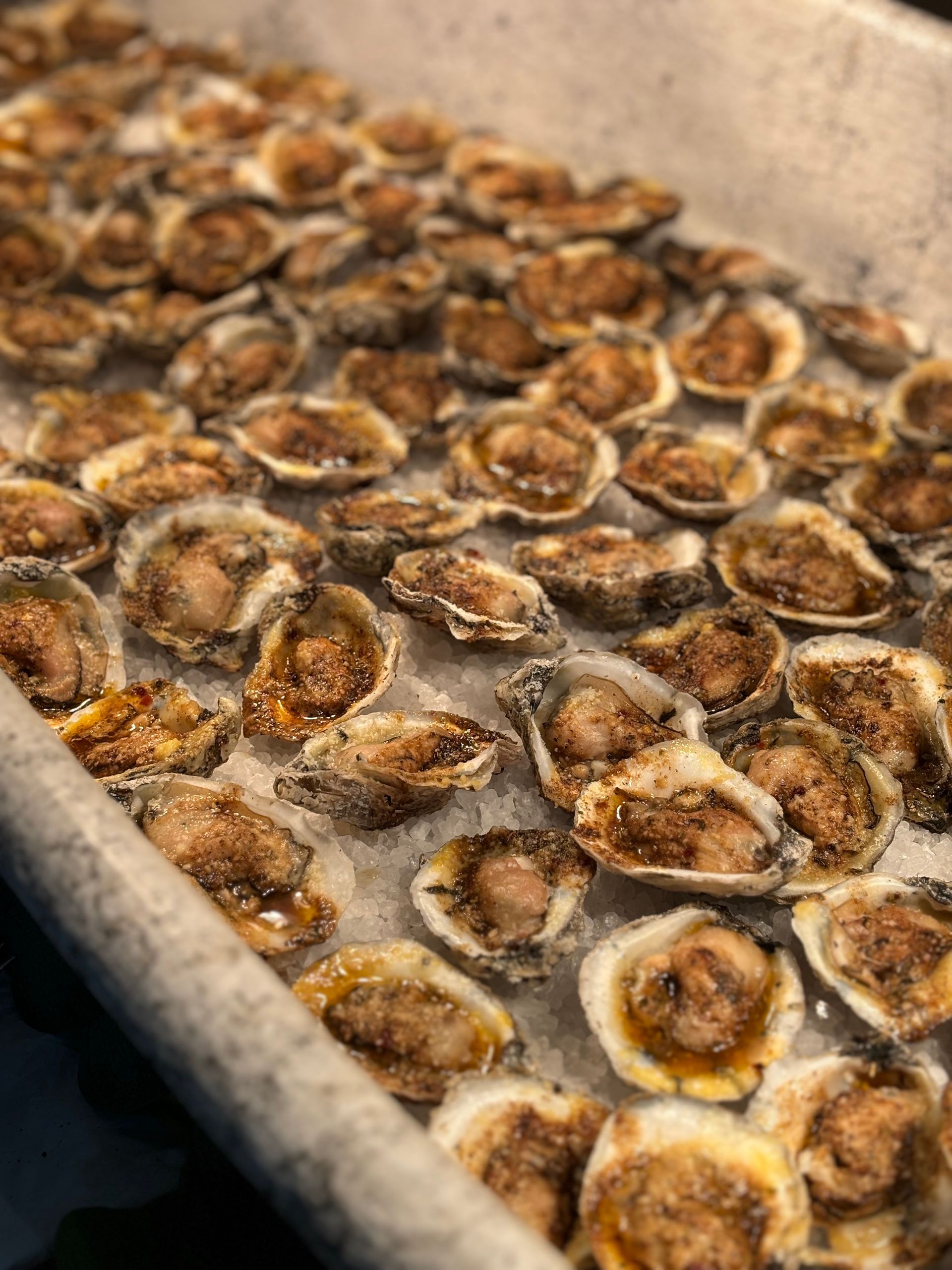 A tray of raw oysters on ice, ready to be served, with seasoning visible.
