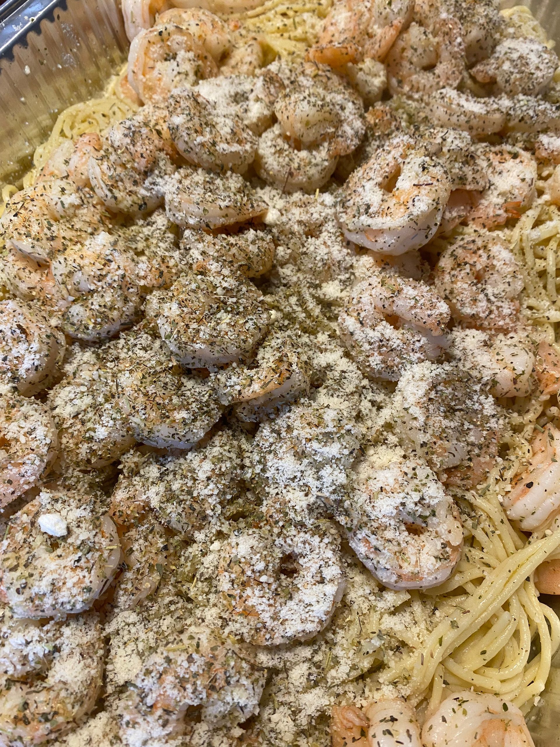 Shrimp scampi over spaghetti, seasoned with herbs and spices, in a foil container.