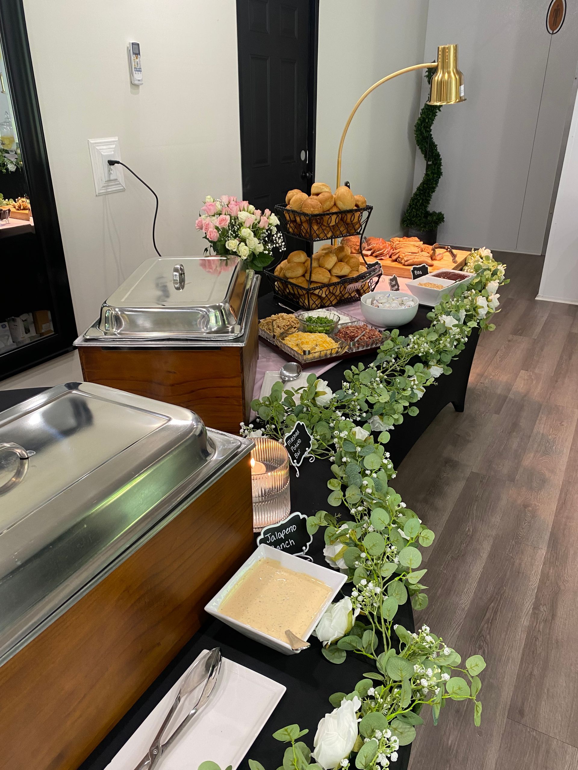 A buffet table with chafing dishes, baskets of food, and floral arrangements. Catering setting with various dishes.