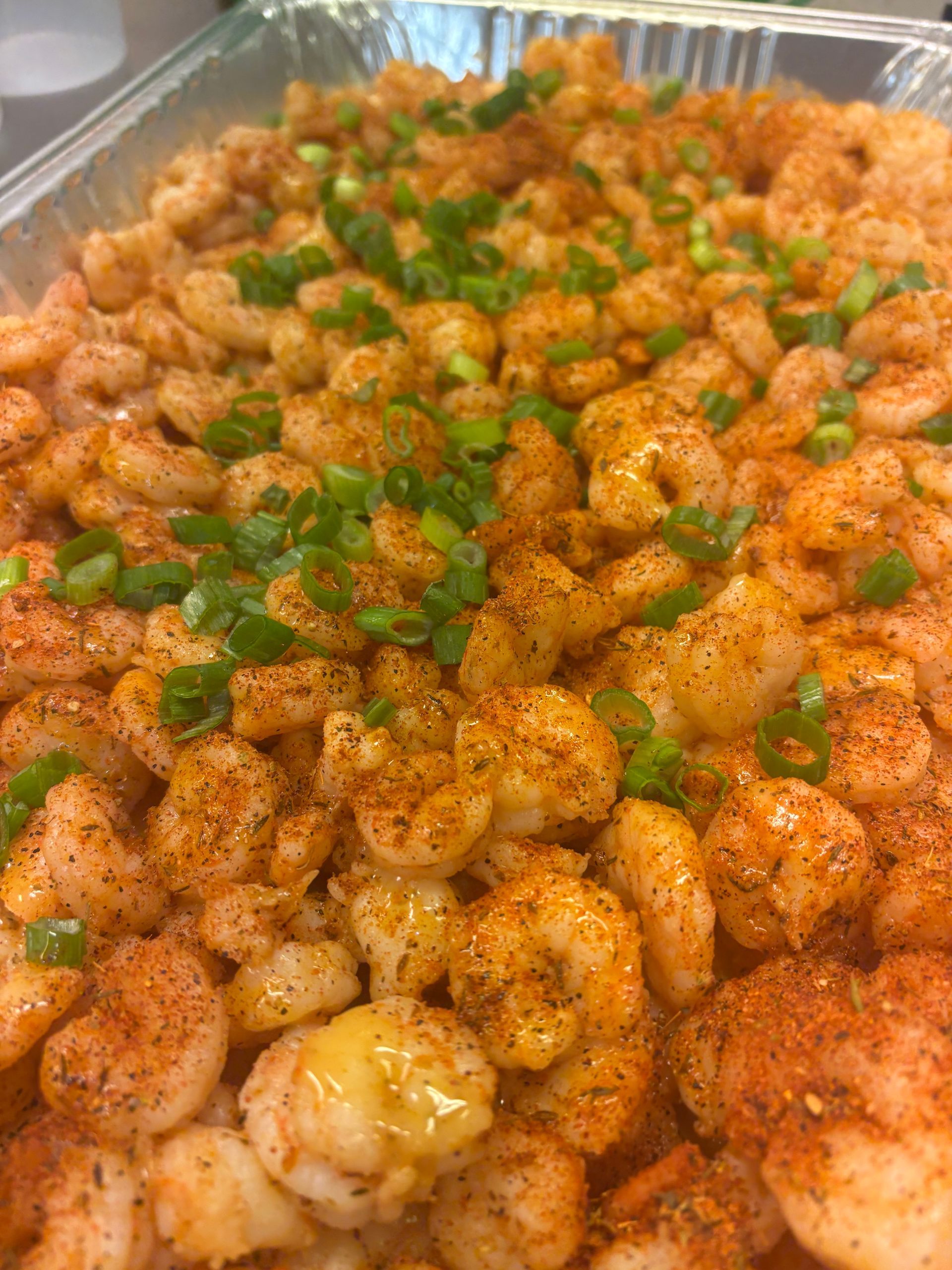 A tray of cooked shrimp seasoned with spices and topped with chopped green onions.
