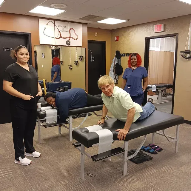 Massage therapy class with students practicing on tables in a clinic training room.