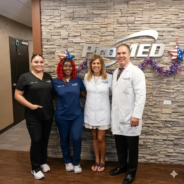 Four staff members posing in front of a stone wall and company logo, dressed in black, blue, white, and a lab coat.
