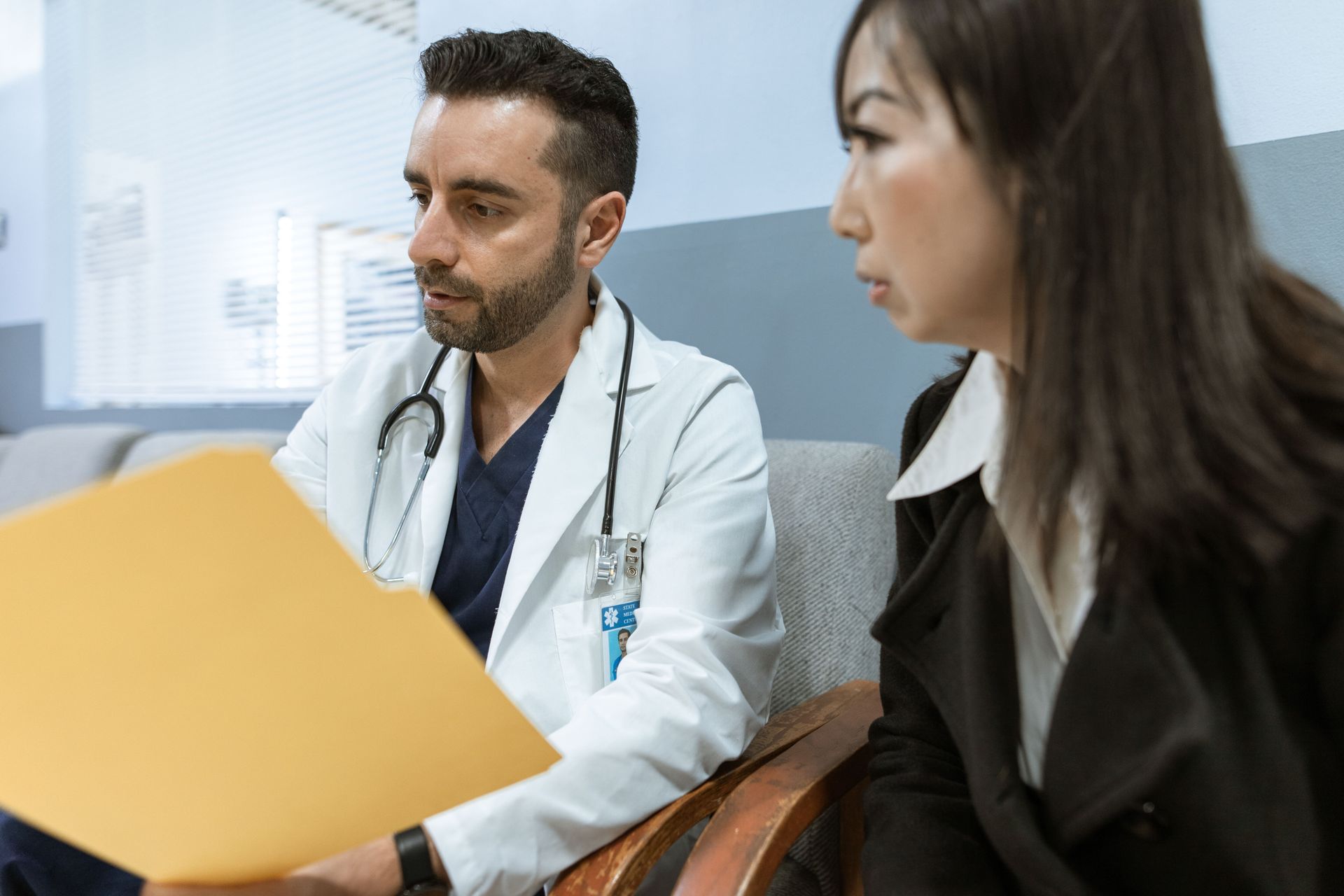 Doctor reviewing a file with a seated colleague in a bright office