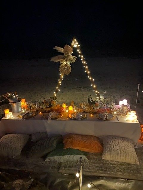 Beach set up, wood triagle piece featured lights and a bo ho flower bouquet. Low table,flowers, candles, lush pillows.