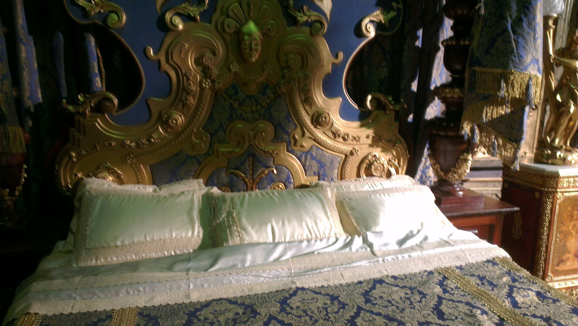 An upholstered bed head and three ornate pillows. Made for