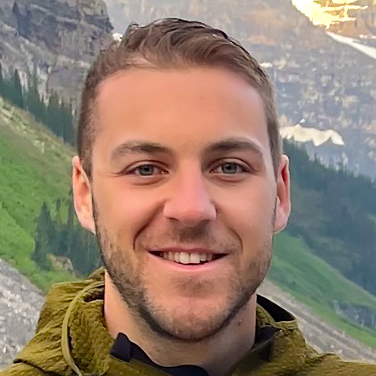 Un homme avec une barbe sourit devant une montagne.