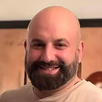 Un homme chauve avec une barbe sourit à la caméra.