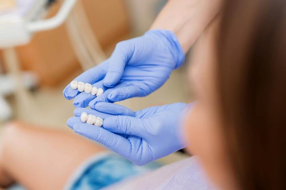 Dental crown being placed on a prepared tooth. Illustration shows the procedure, pink gums, and surrounding teeth.