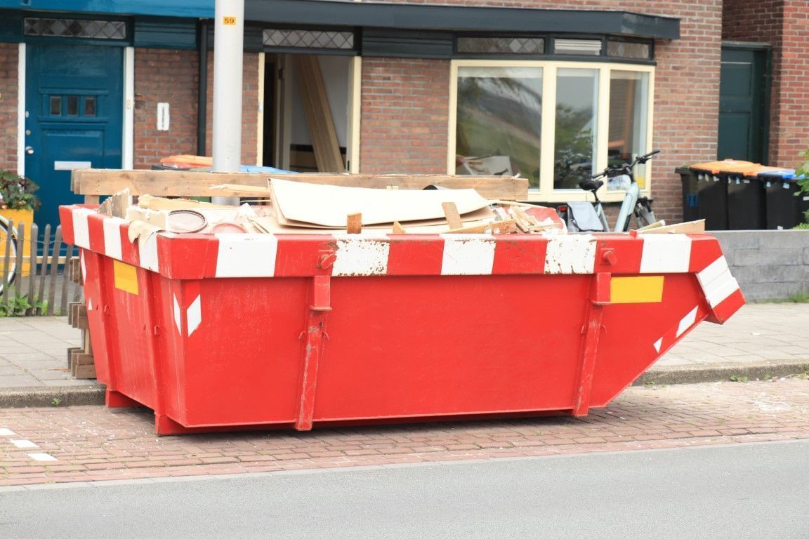 Red construction dumpster filled with debris on a street in front of a brick building