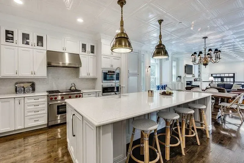 A kitchen with white cabinets , stainless steel appliances , a large island and stools.