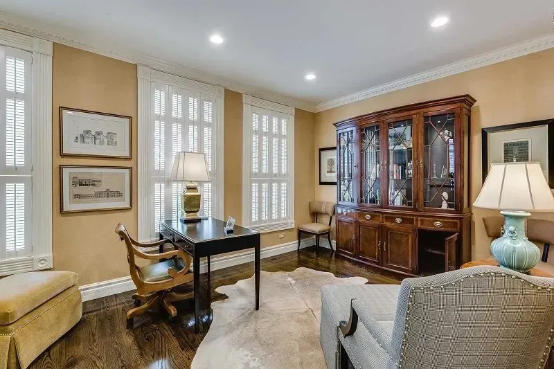 A living room with a desk , chairs , lamps and a hutch.