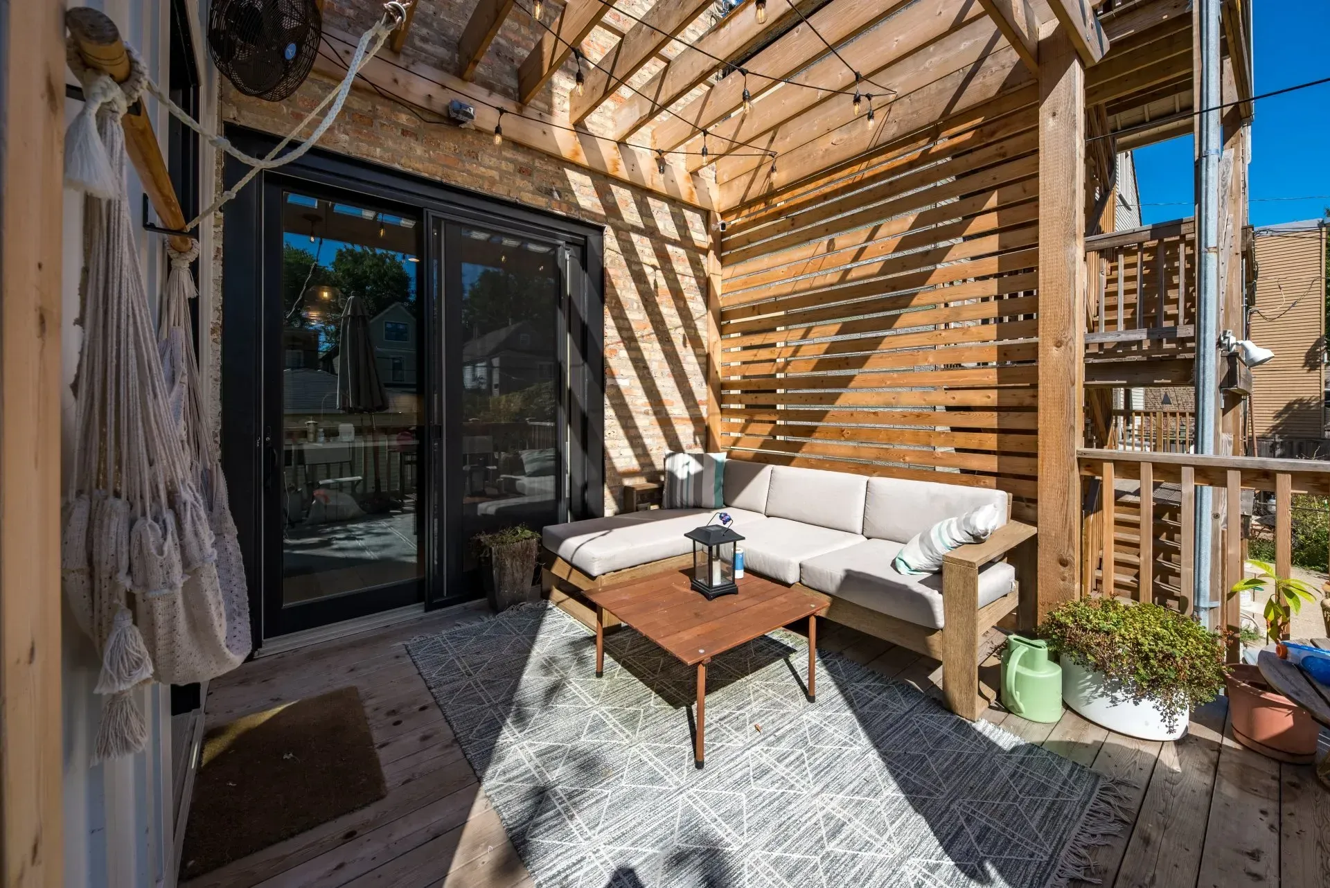 A wooden deck with a couch and a coffee table under a pergola.