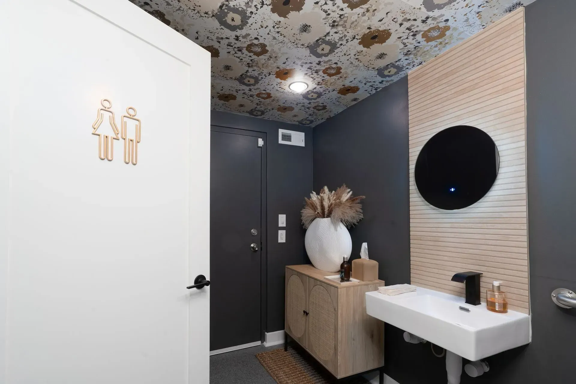 A bathroom with a sink , mirror and door.