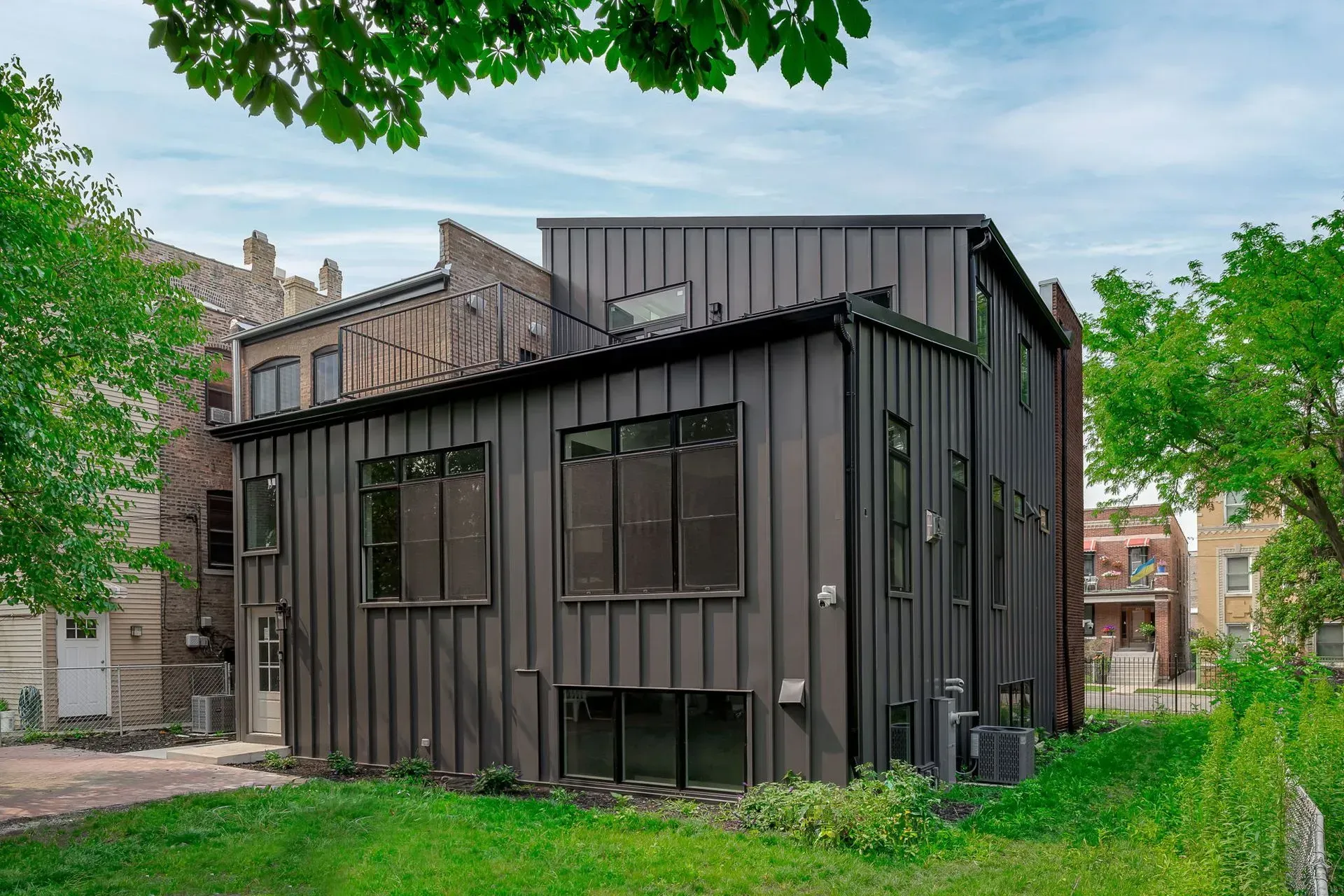 A large black house with a lot of windows is sitting on top of a lush green field.