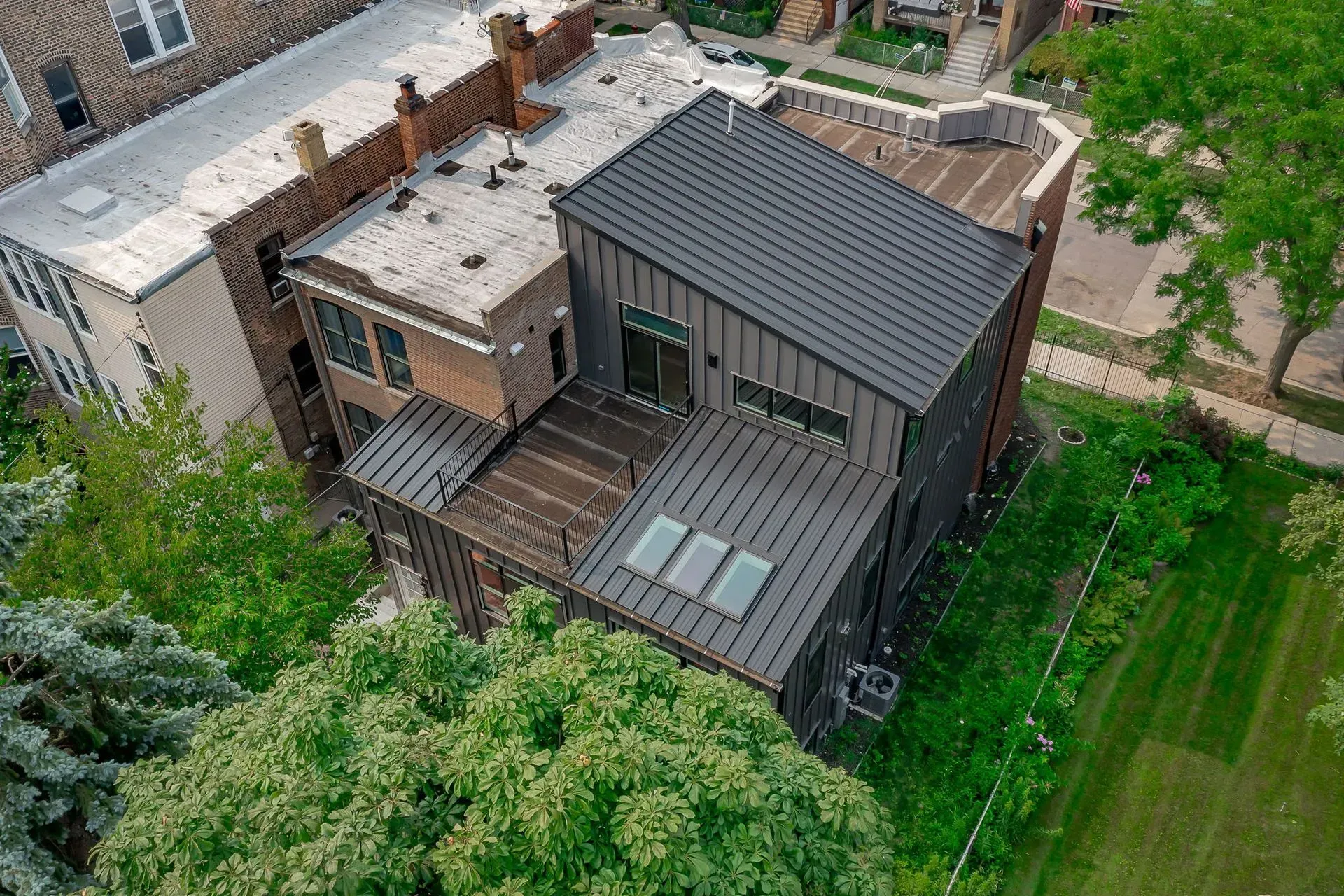 An aerial view of a large house with a roof that is surrounded by trees.