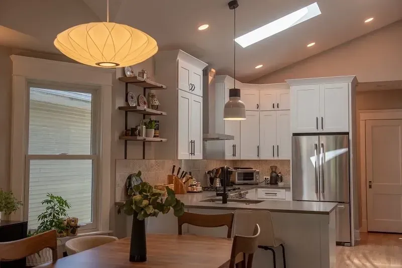 A kitchen with white cabinets , a stainless steel refrigerator , a table and chairs.