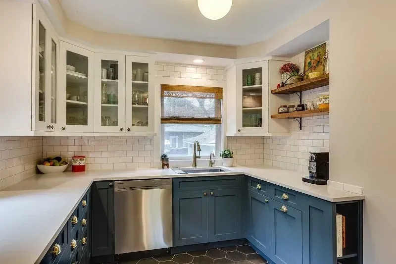 A kitchen with blue cabinets , white counter tops , stainless steel appliances and a window.