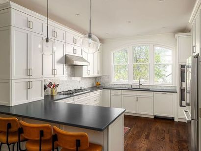A kitchen with white cabinets , black counter tops , stainless steel appliances and hardwood floors.
