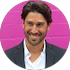 A man in a suit and white shirt is smiling in front of a pink wall.