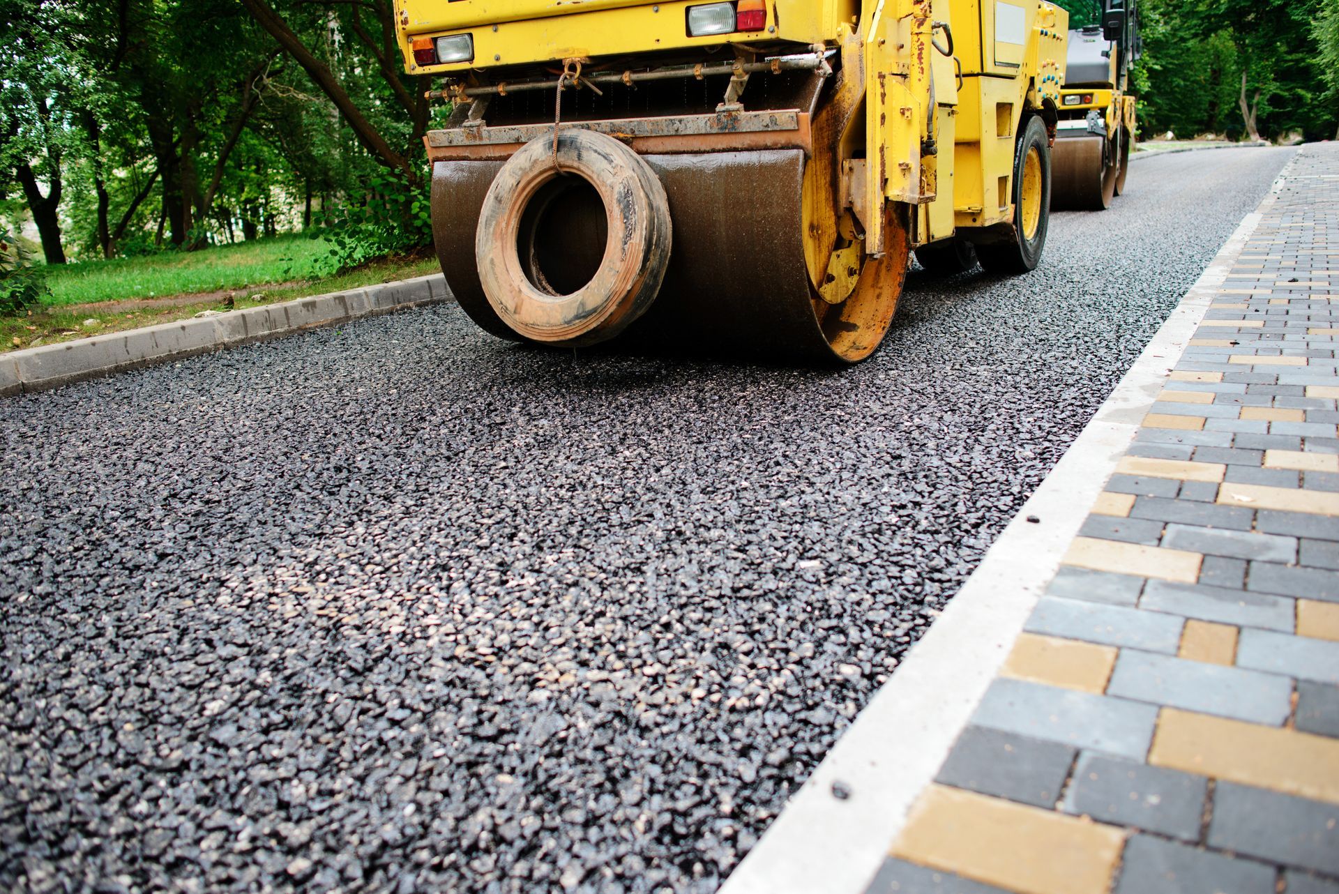 Road roller paving fresh asphalt beside a tiled sidewalk Road roller paving fresh asphalt beside a tiled sidewalk