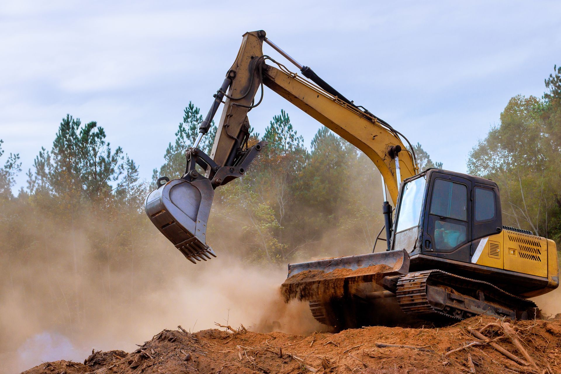 Yellow excavator digging dirt, kicking up dust at a construction site.