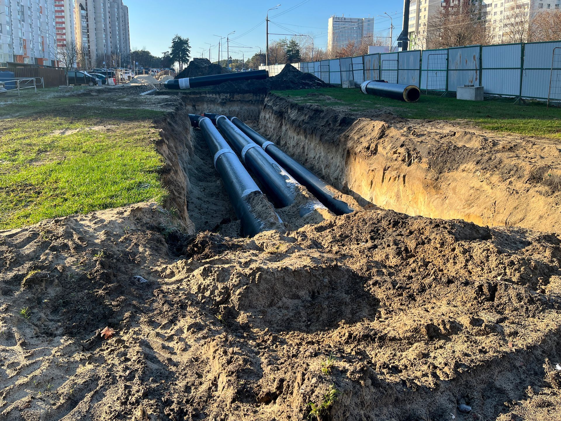 Trenches with large underground pipes beside a muddy construction site in a city neighborhood Trenches with large underground pipes beside a muddy construction site in a city neighborhood