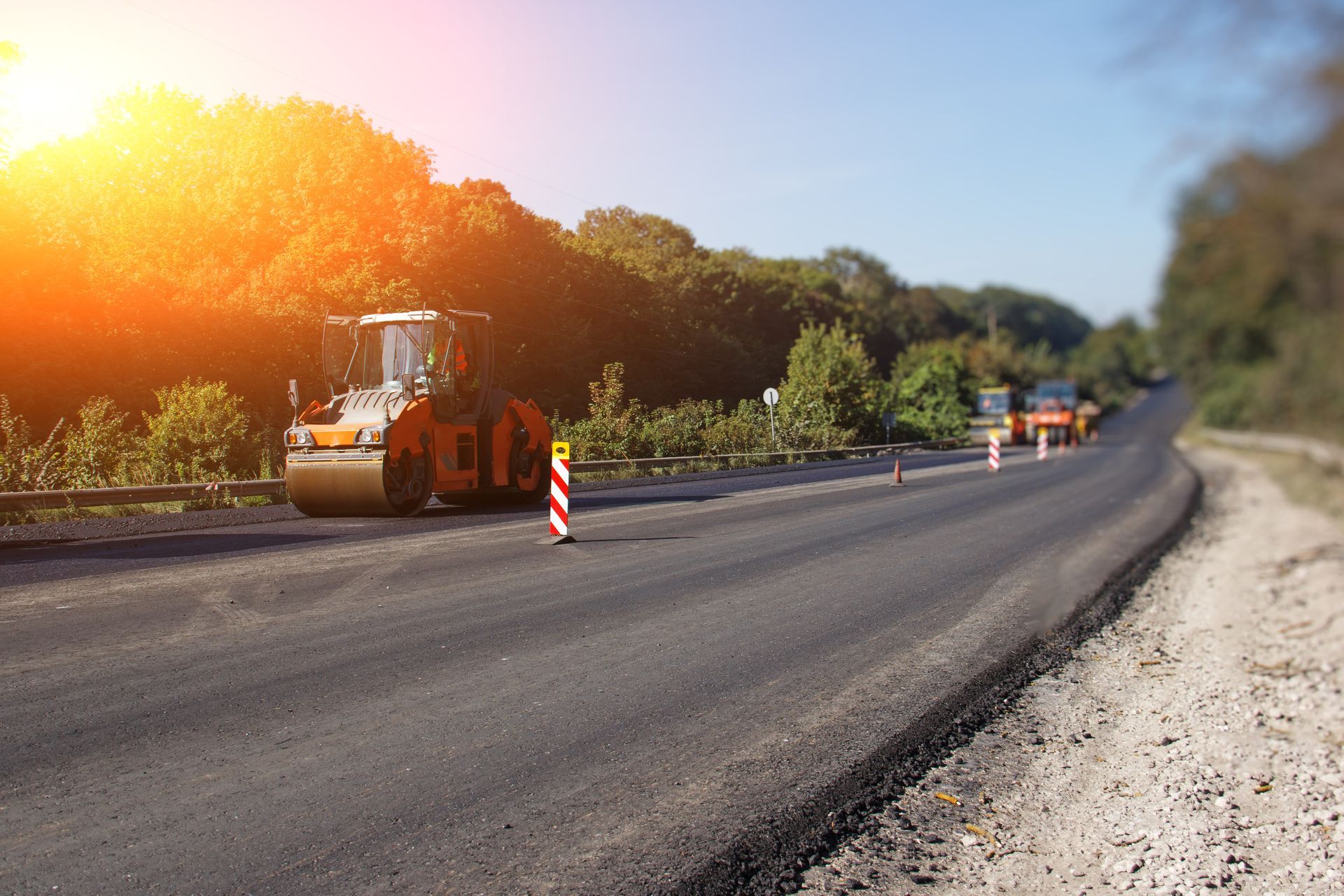 Road construction crew with rollers and traffic cones on a sunlit asphalt road in a rural area Road construction crew with rollers and traffic cones on a sunlit asphalt road in a rural area