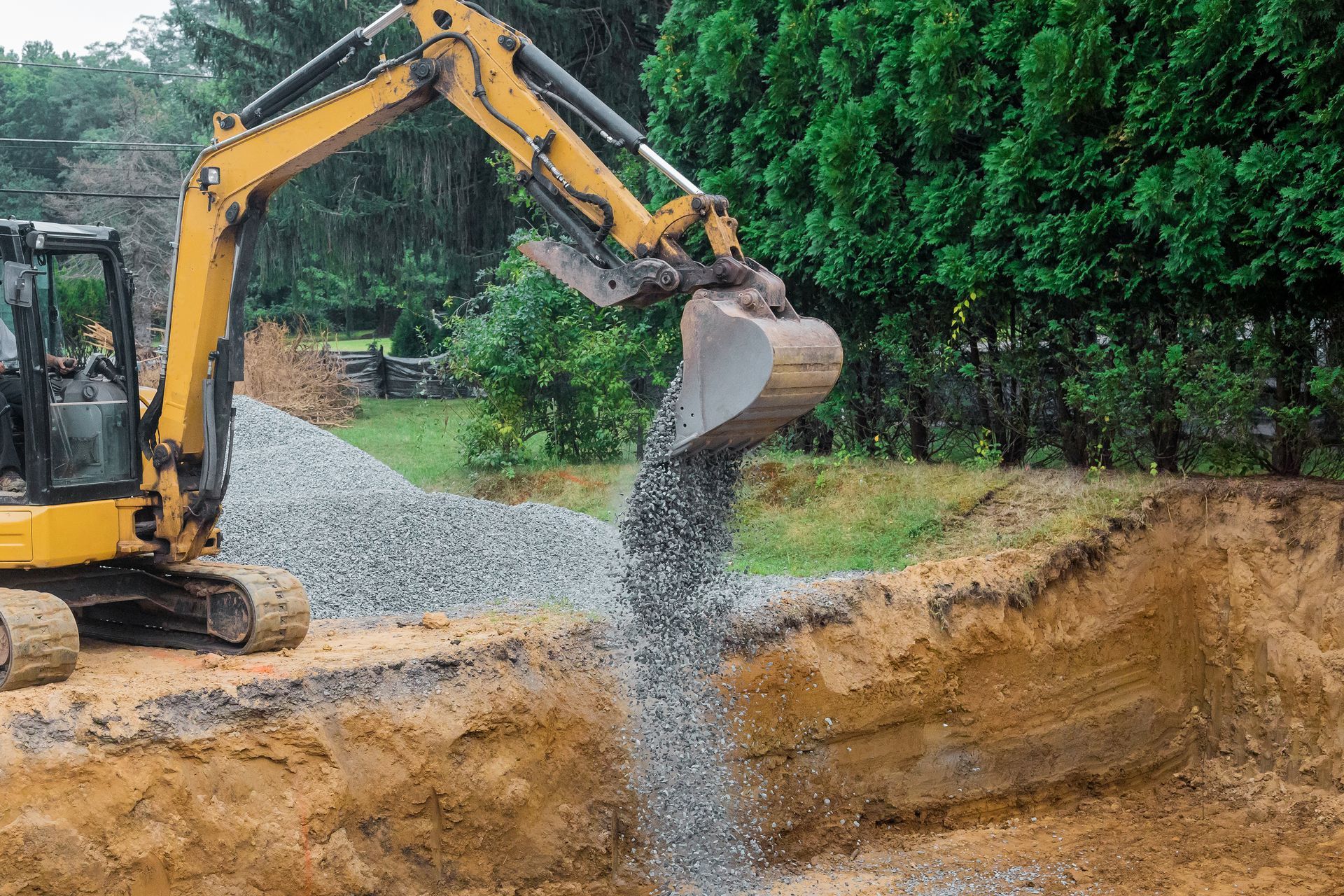 Yellow excavator dumping gravel into a trench at a construction site outdoors Yellow excavator dumping gravel into a trench at a construction site outdoors