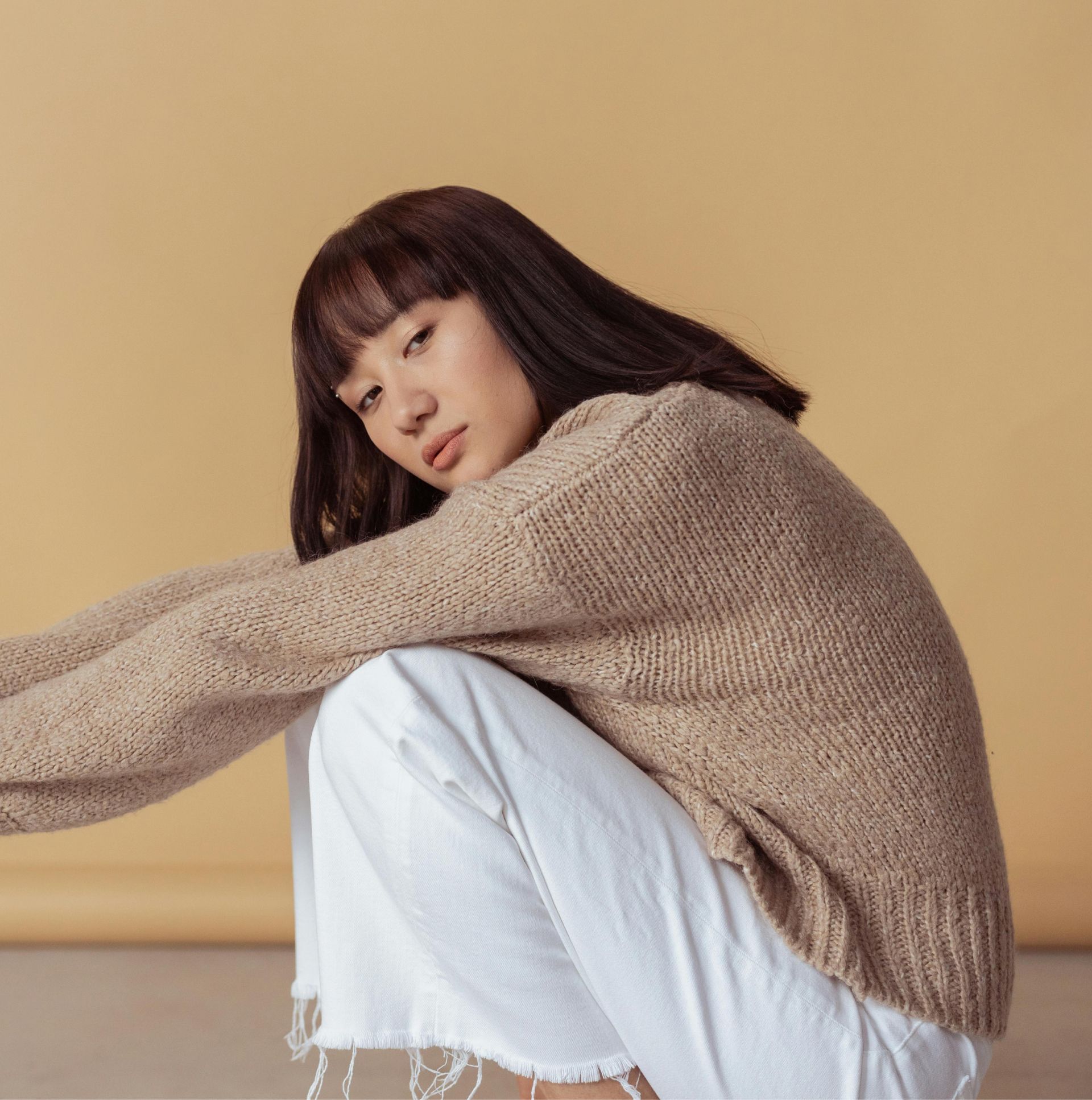 A woman is wearing a brown sweater and white jeans.