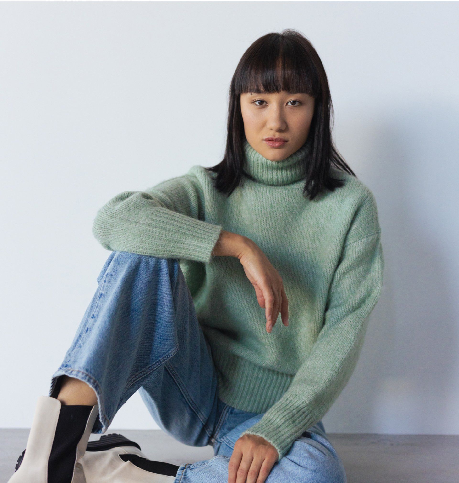A woman in a green sweater covering her face with her hands
