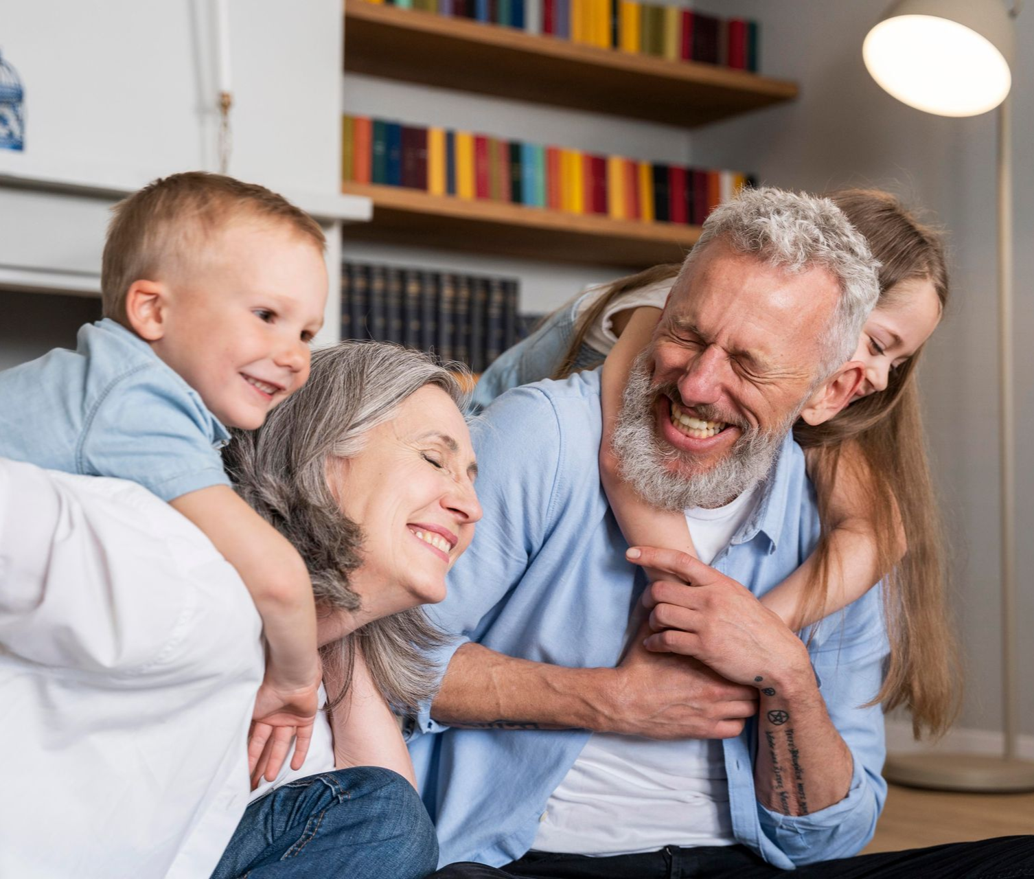 Grandparents and grandchildren laugh together on the floor in a home, embracing and smiling.