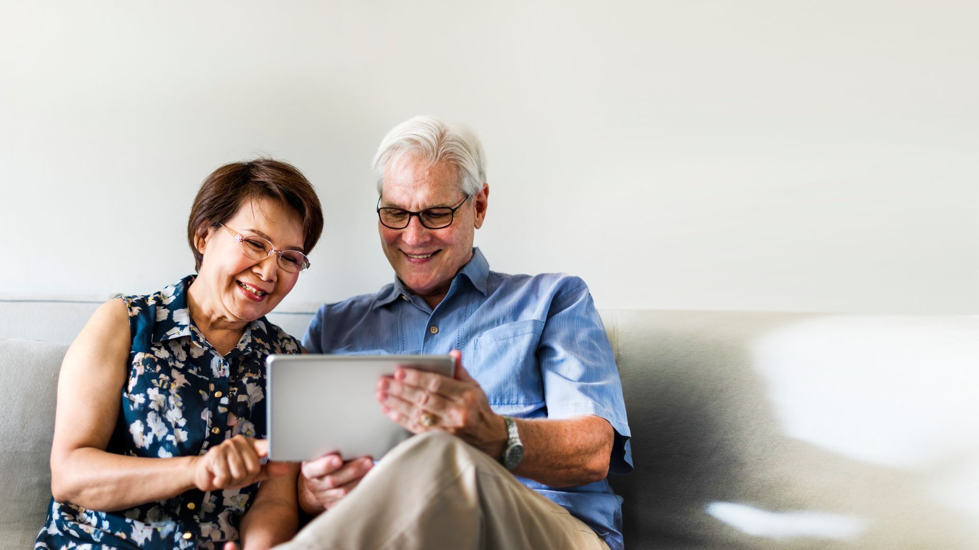 Smiling couple looking at a tablet on a light-colored couch.
