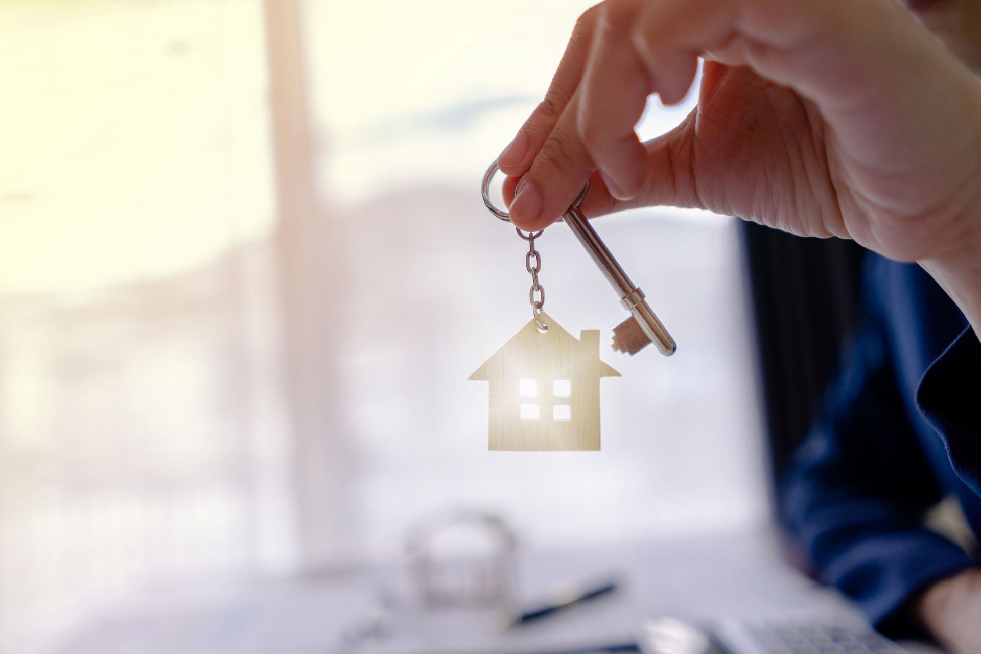 A person is holding a key with a house keychain attached to it.