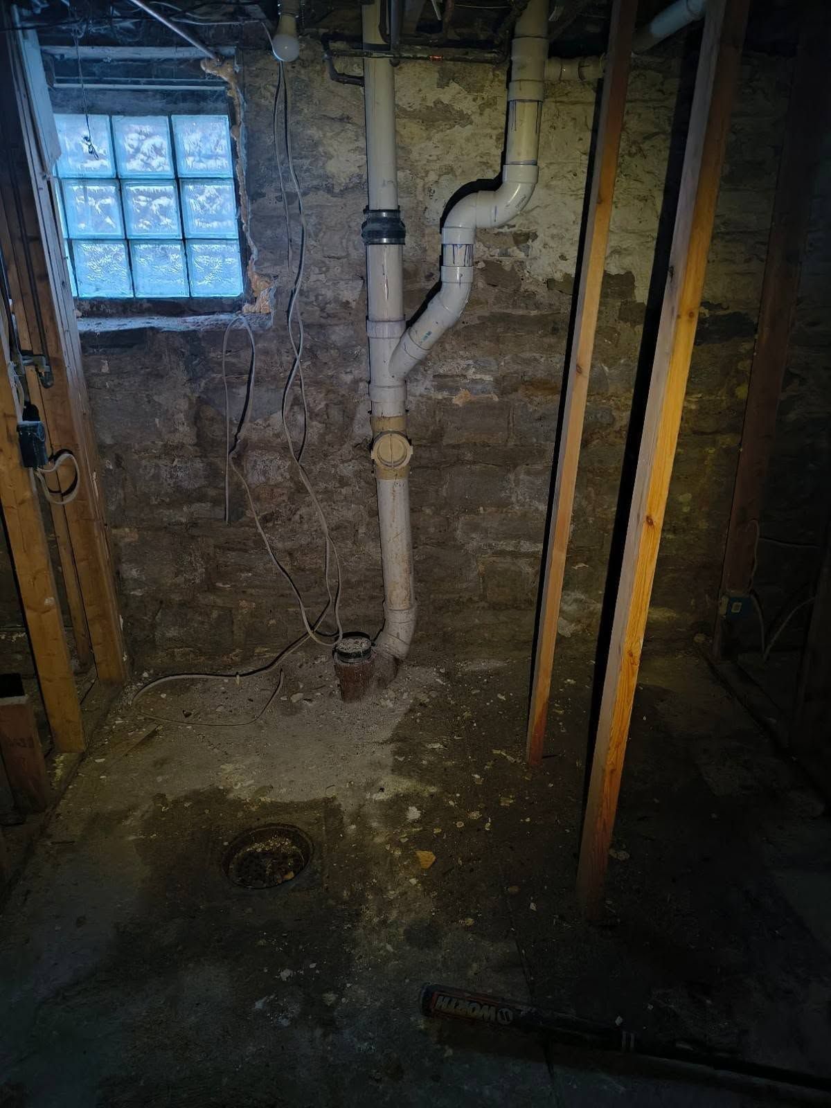 Basement with exposed plumbing, stone walls, small window, and a dirt floor.