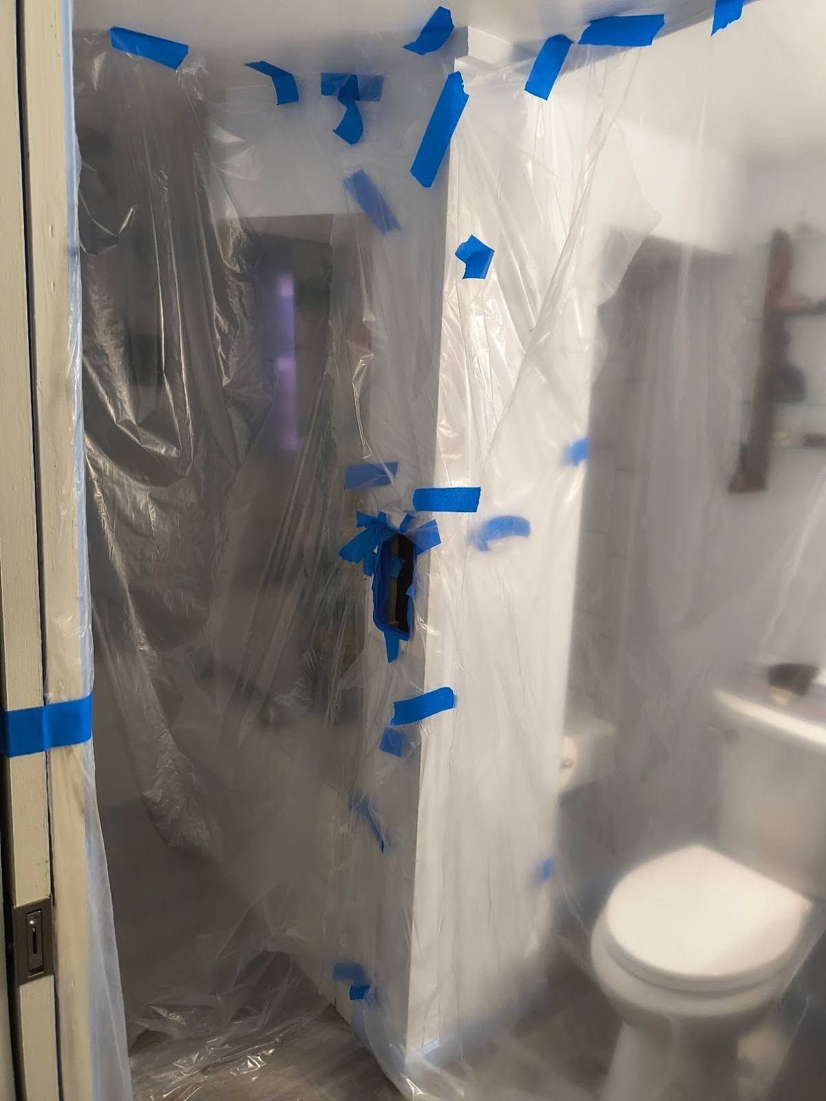 Bathroom under renovation, with shower wrapped in plastic and blue painter’s tape around the doorway.
